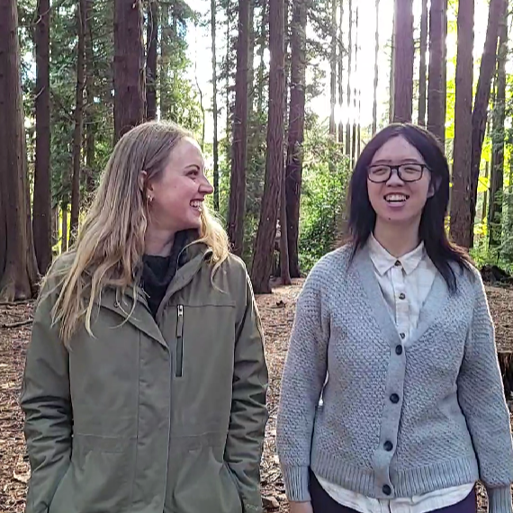 Two people walking side-by-side in a forested area.